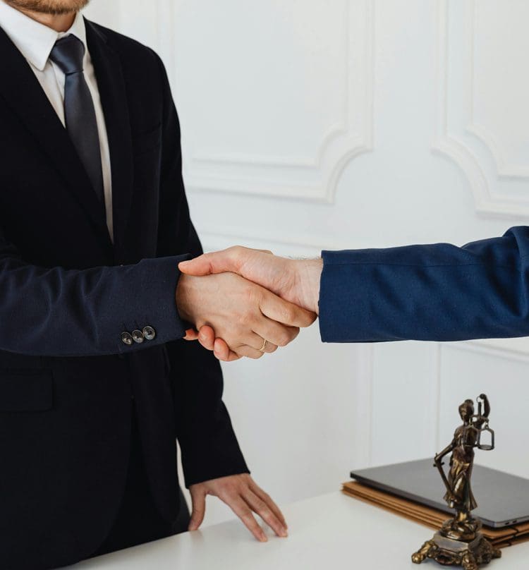 Two men in suits shaking hands over a table.